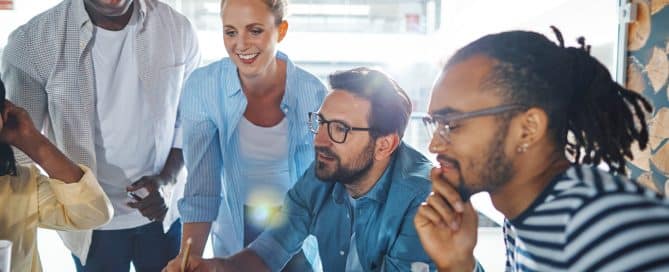 Diverse group of smiling businesspeople going over paperwork together during a meeting inside of a glass office